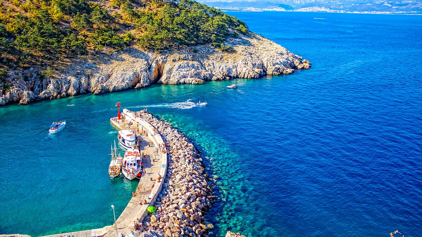 Båtar vid en stenpir i en turkos vik längs Kroatiens klippiga kust