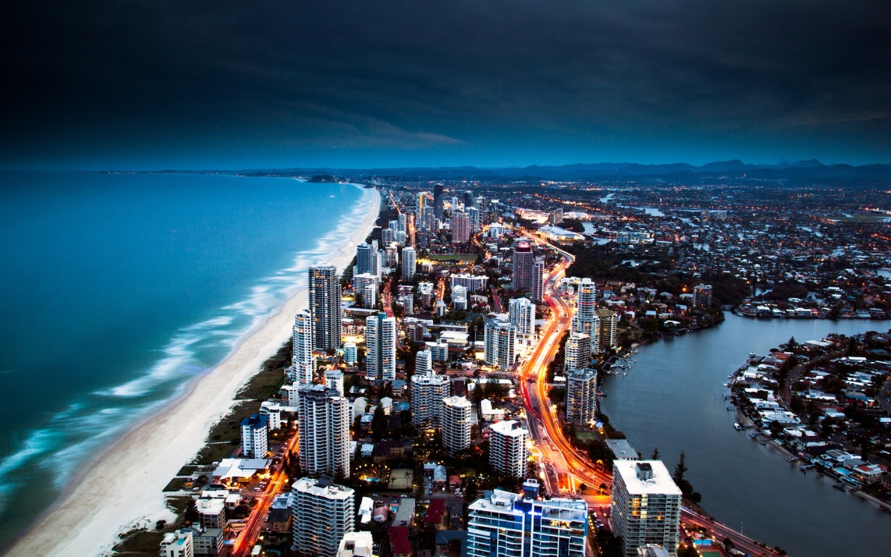 Gold Coasts upplysta skyline mellan strand och kanaler i Australien